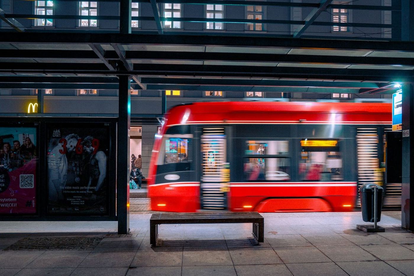 A red tram streaks through a Polish city station at night, capturing the motion of urban life.