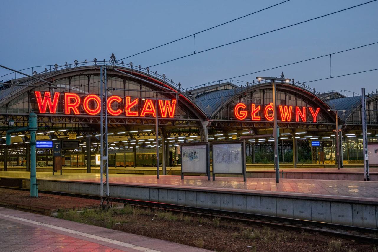 The iconic red neon sign of Wrocław Główny railway station glowing at dusk above the platforms