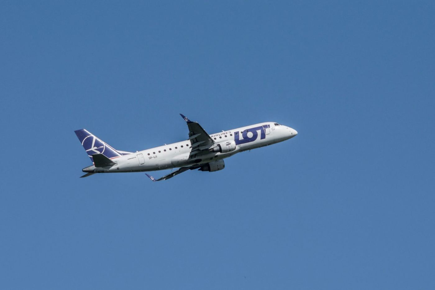 A LOT Polish Airlines Embraer 175 aircraft climbing against a clear blue sky, seen from a side profile with the navy crane tail logo visible.
